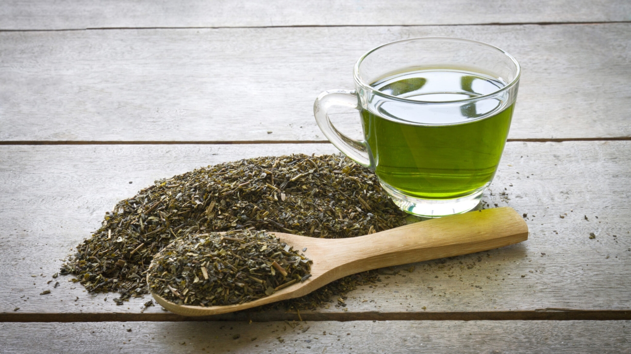 cup of green tea and spoon of dried green tea leaves on wooden background